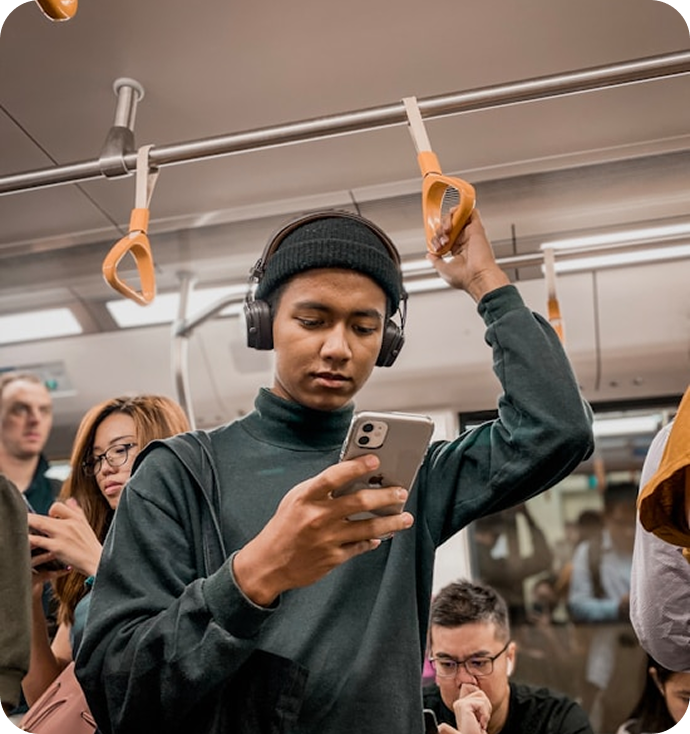 A young commuter wearing headphones looks at their phone on a train
